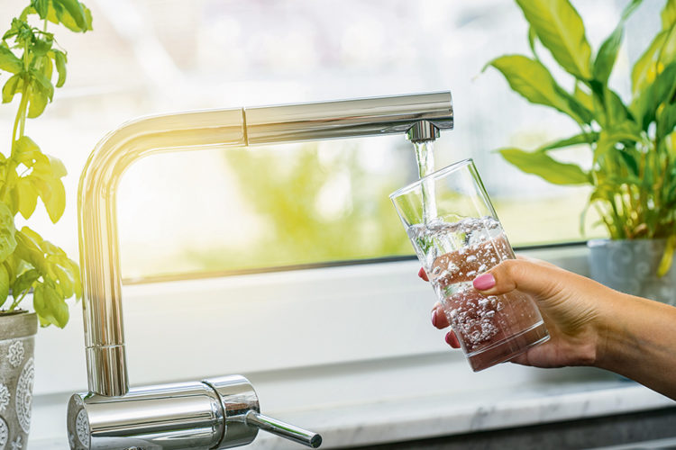 A glass being filled with clean, clear filtered water from a modern kitchen faucet